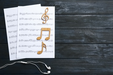 Flat lay composition with music notes, earphones and space for text on wooden background