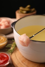 Photo of Fondue pot, fork with piece of raw meat and other products on table, closeup