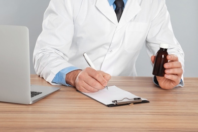 Photo of Professional pharmacist working at table against light grey background, closeup