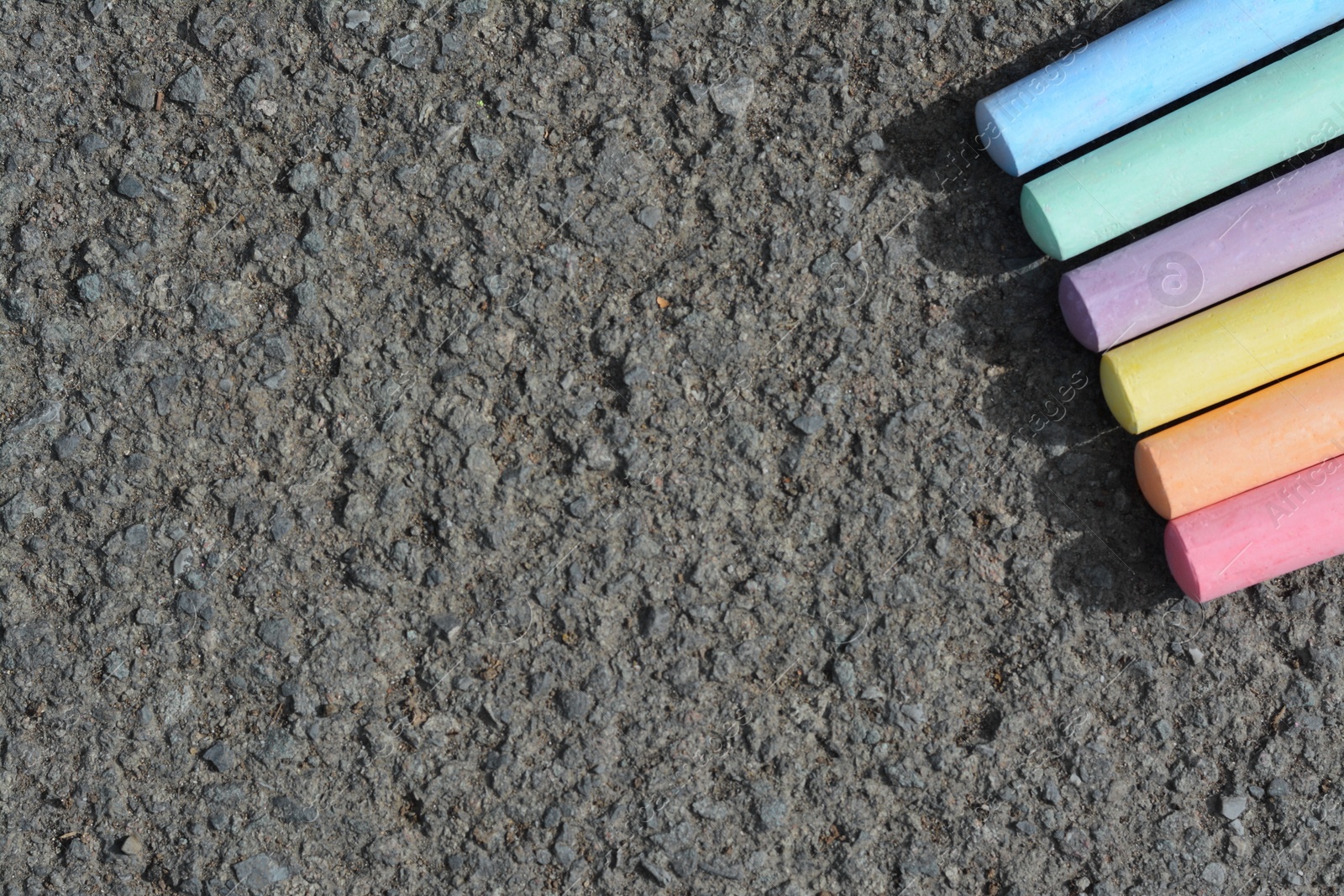 Photo of Colorful chalk sticks on asphalt, flat lay. Space for text