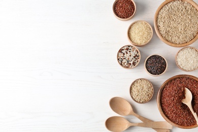 Photo of Flat lay composition with brown and other types of rice on white wooden background. Space for text