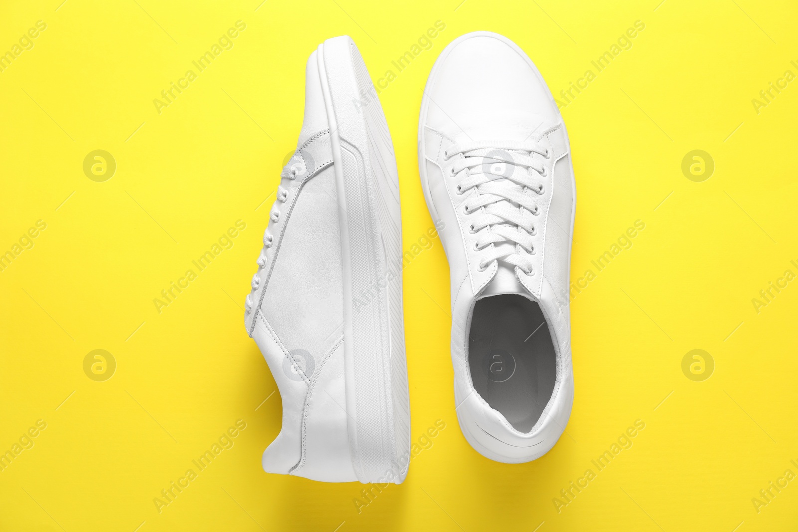 Photo of Pair of stylish white sneakers on yellow background, top view