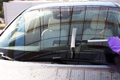 Worker cleaning automobile windshield with squeegee at car wash