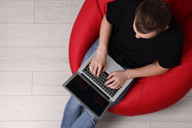 Photo of Man working with laptop in beanbag chair, top view. Space for text
