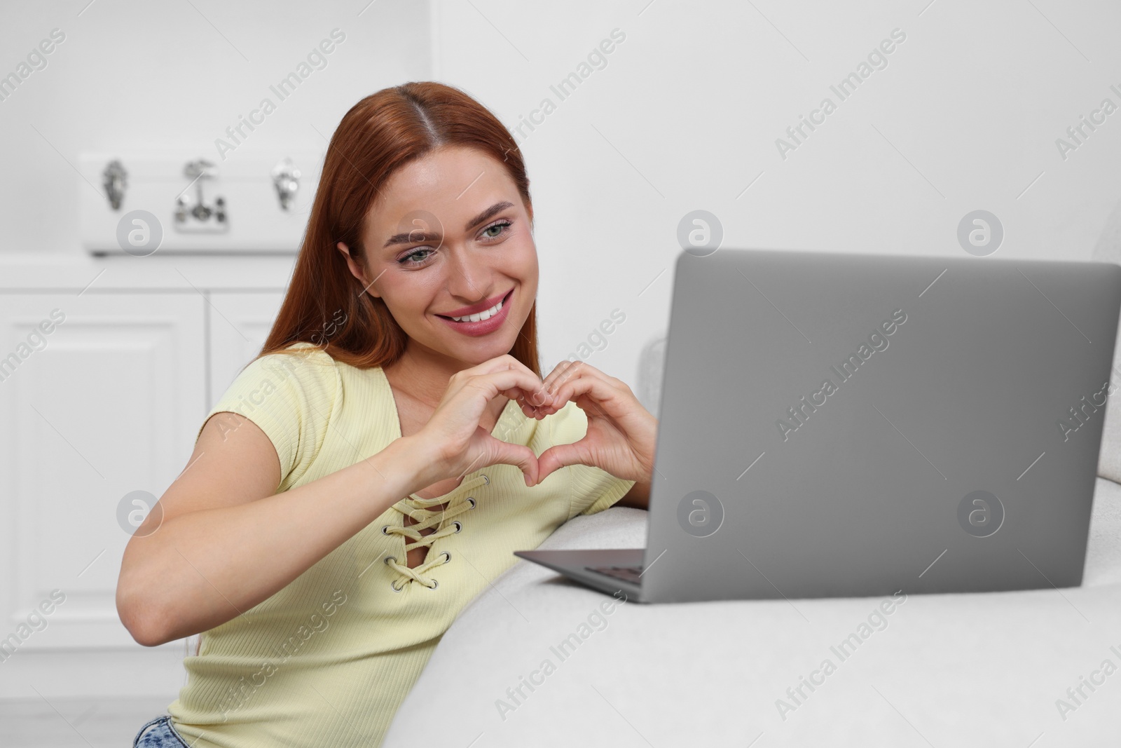 Photo of Woman making heart with hands during video chat via laptop at home. Long-distance relationship