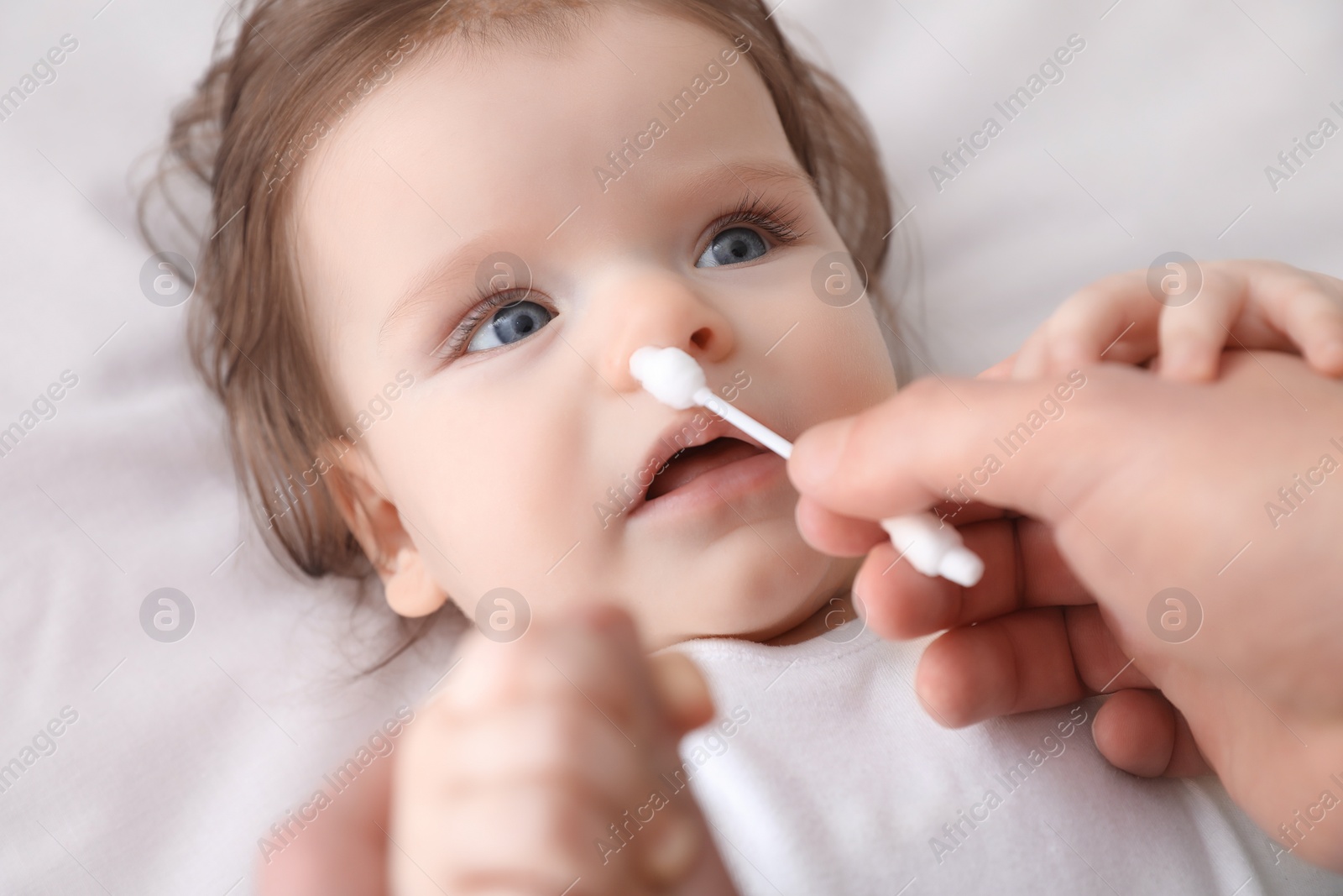 Photo of Father cleaning nose of his baby with cotton bud on bed, closeup