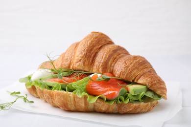 Photo of Tasty croissant with salmon, avocado, mozzarella and lettuce on white table, closeup