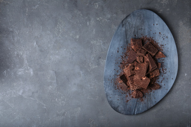 Photo of Pieces of dark chocolate on grey table, top view. Space for text