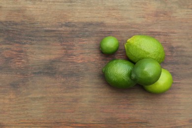 Photo of Fresh ripe limes on wooden table, flat lay. Space for text
