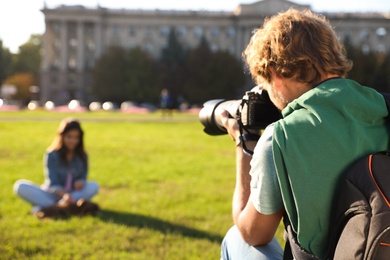 Male photographer taking photo of young woman with professional camera on grass outdoors