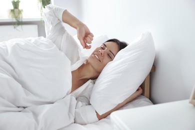 Happy young woman lying on soft pillow in bed at home