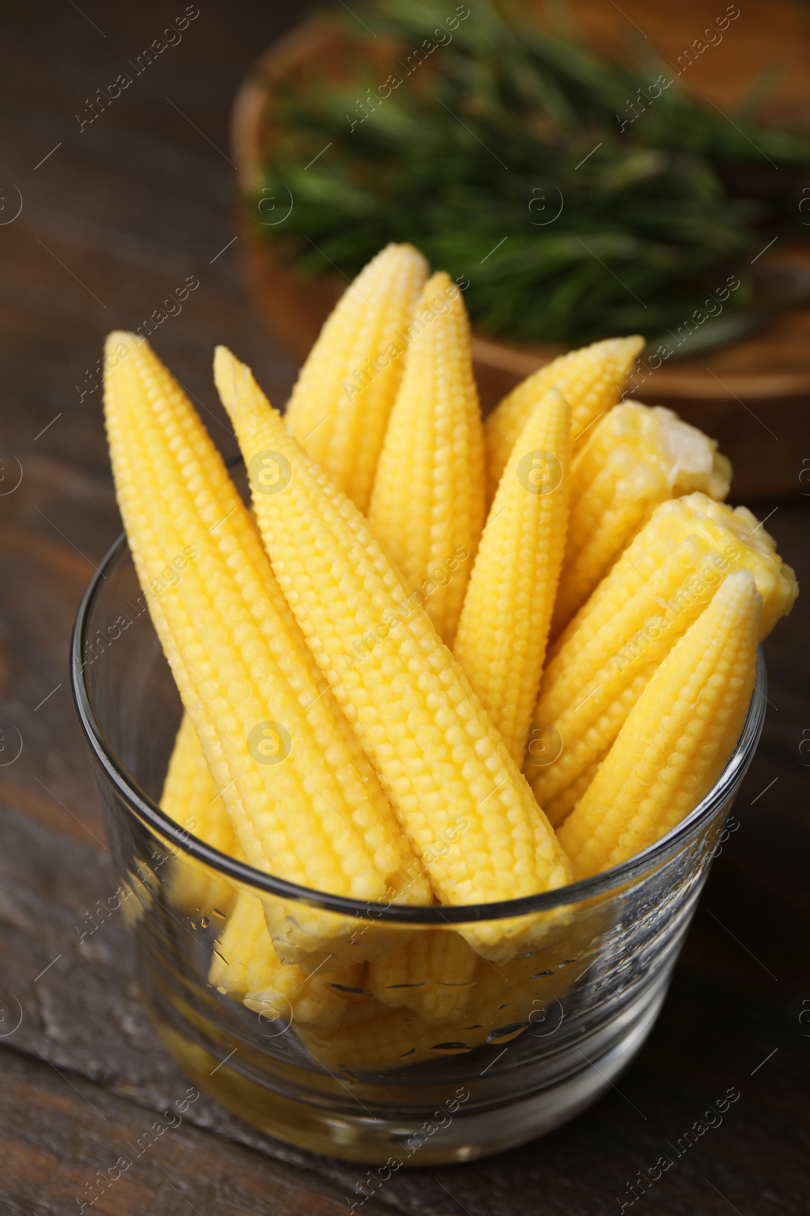 Photo of Tasty fresh yellow baby corns in glass on wooden table