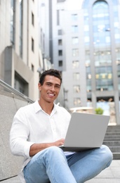 Photo of Handsome young African-American man with laptop sitting on stairs outdoors