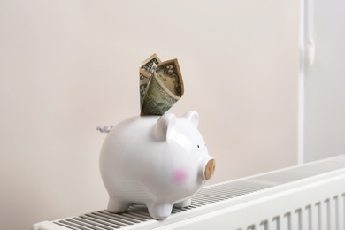 Photo of Piggy bank with money on heating radiator indoors