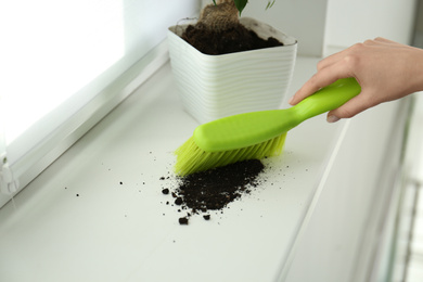 Photo of Woman sweeping away scattered soil from window sill with brush, closeup