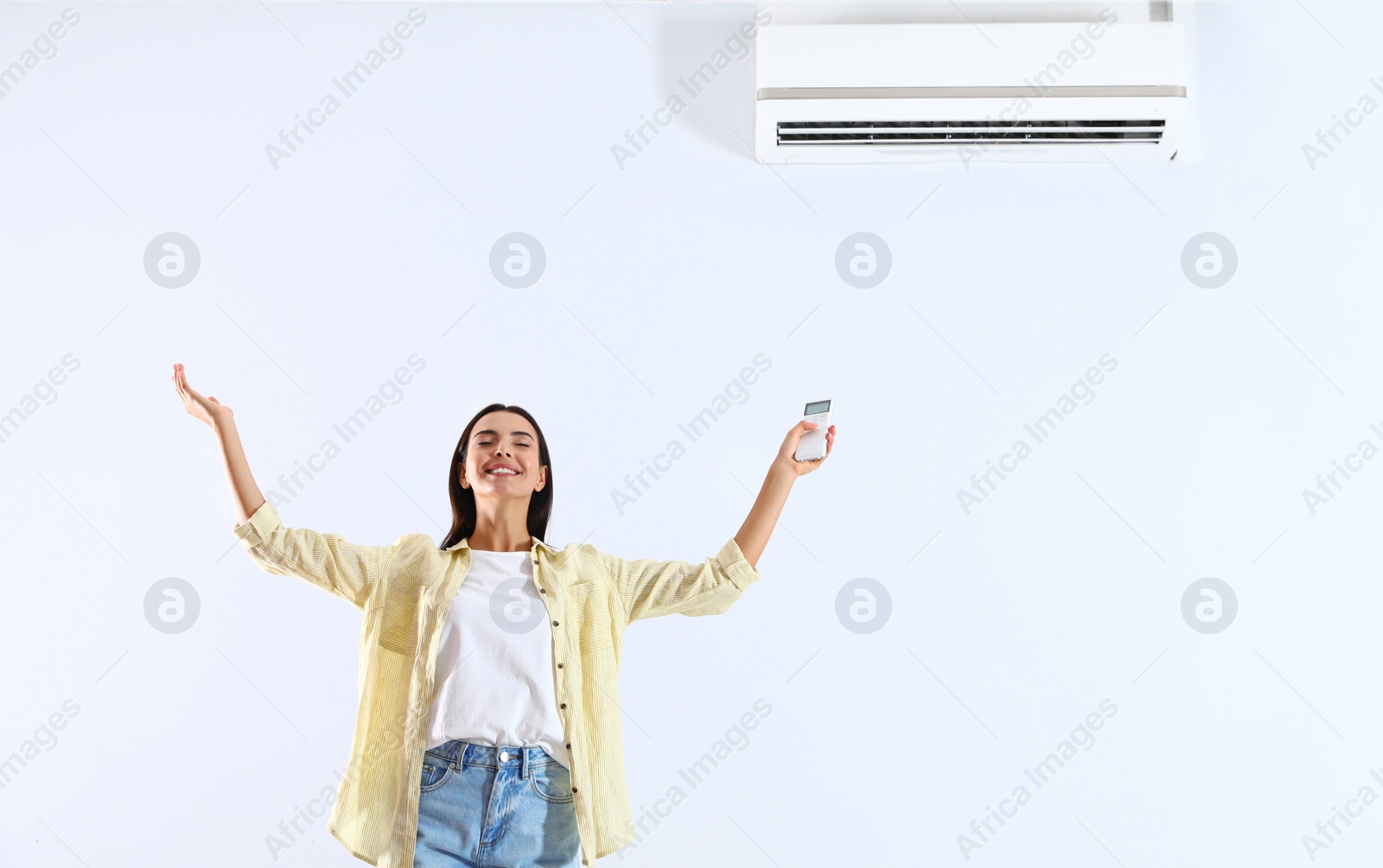 Photo of Young woman with air conditioner remote on white background