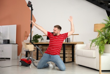 Photo of Young man having fun while vacuuming at home