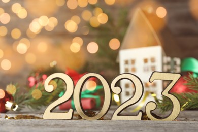 Number 2023 and festive decor on wooden table, closeup. Bokeh effect