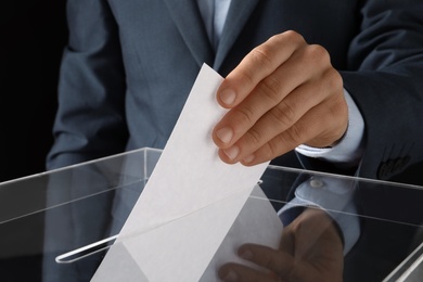 Photo of Man putting his vote into ballot box on black background, closeup