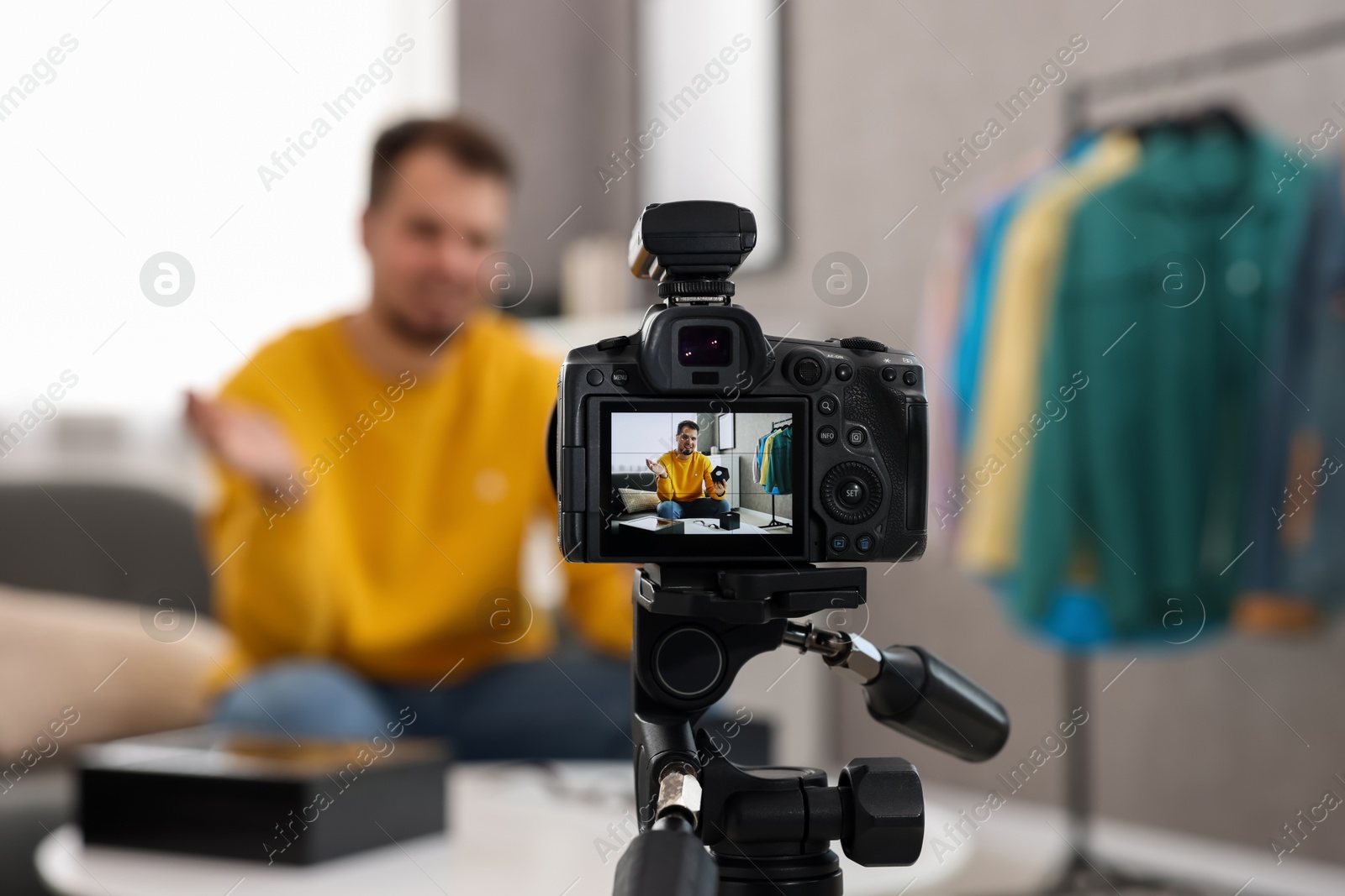 Photo of Fashion blogger showing wristwatch while recording video at home, focus on camera