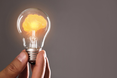 Image of Man holding light bulb with shining brain inside against grey background, space for text. Idea generation