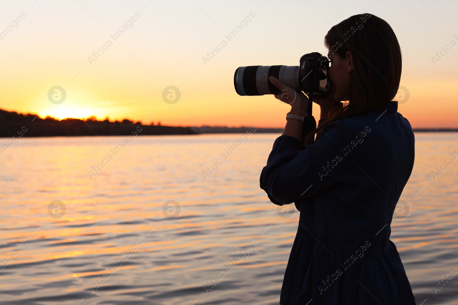 Photo of Young female photographer taking photo of riverside sunset with professional camera outdoors