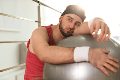 Lazy young man with exercise ball indoors