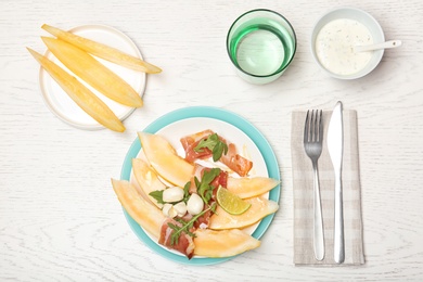 Flat lay composition with melon and prosciutto appetizer served on light table