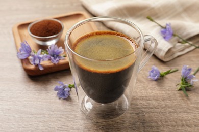 Photo of Glass cup of delicious chicory drink and flowers on wooden table, closeup
