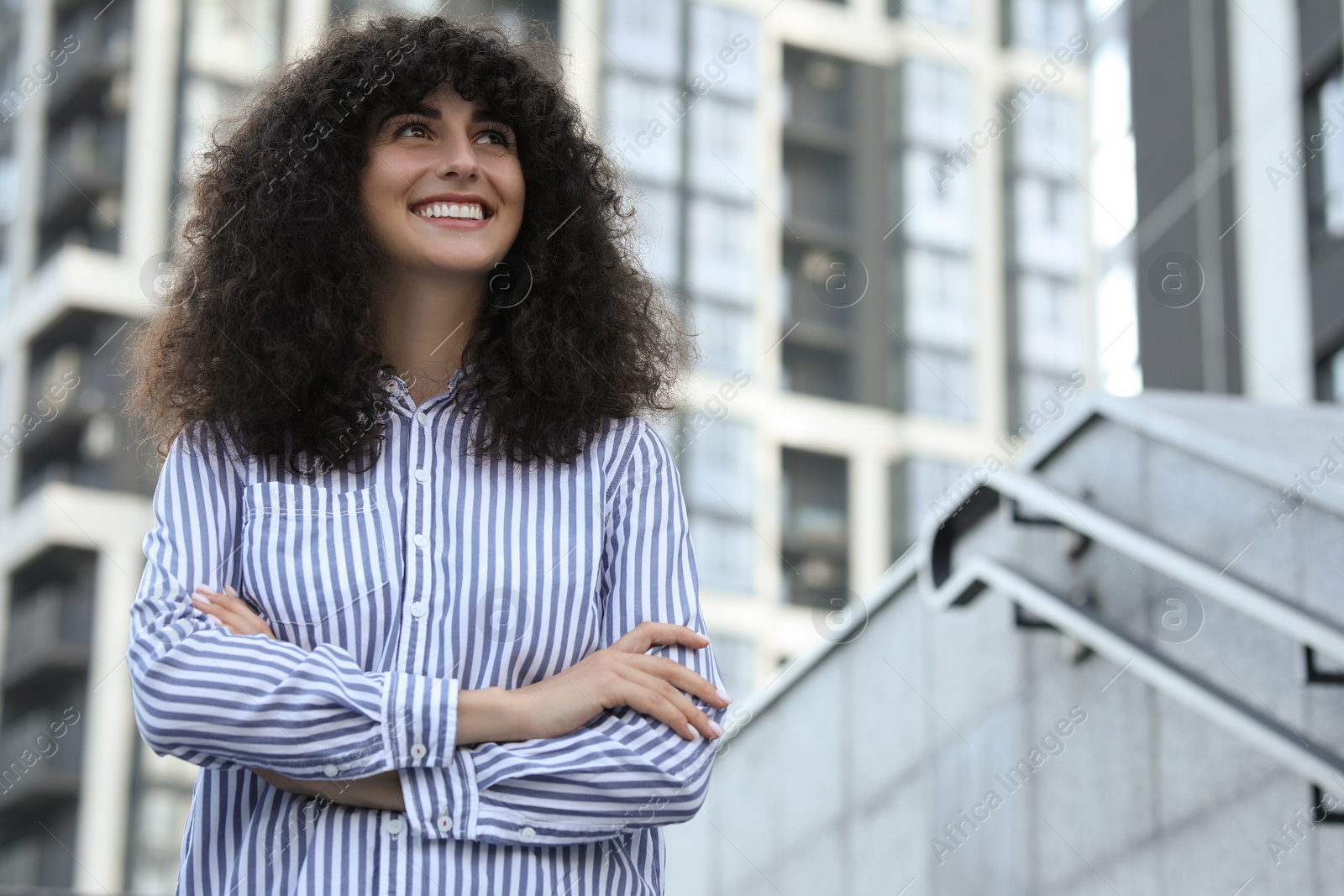 Photo of Portrait of beautiful woman with crossed arms outdoors, low angle view. Attractive lady smiling and posing for camera. Space for text