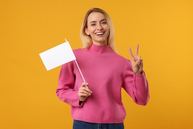 Photo of Happy woman with blank white flag showing V-sign on orange background. Mockup for design
