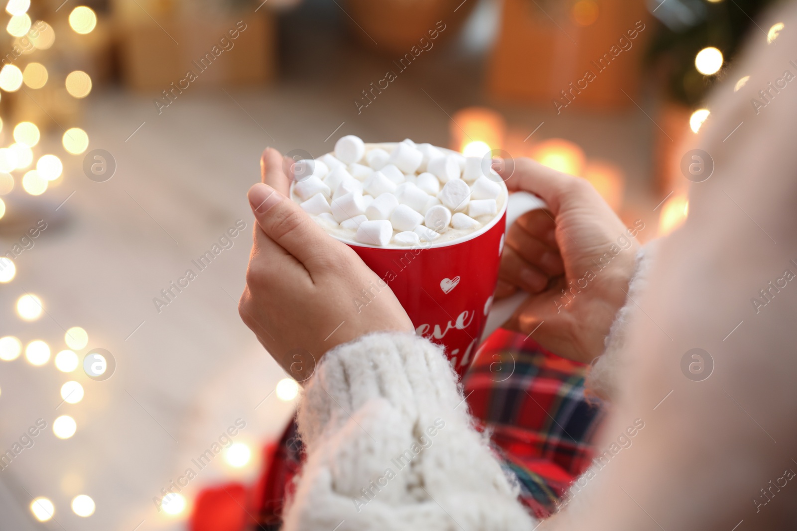 Photo of Woman holding cup of hot drink with marshmallows indoors, closeup. Magic Christmas atmosphere