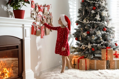 Cute little girl in Santa hat taking gift from Christmas advent calendar at home