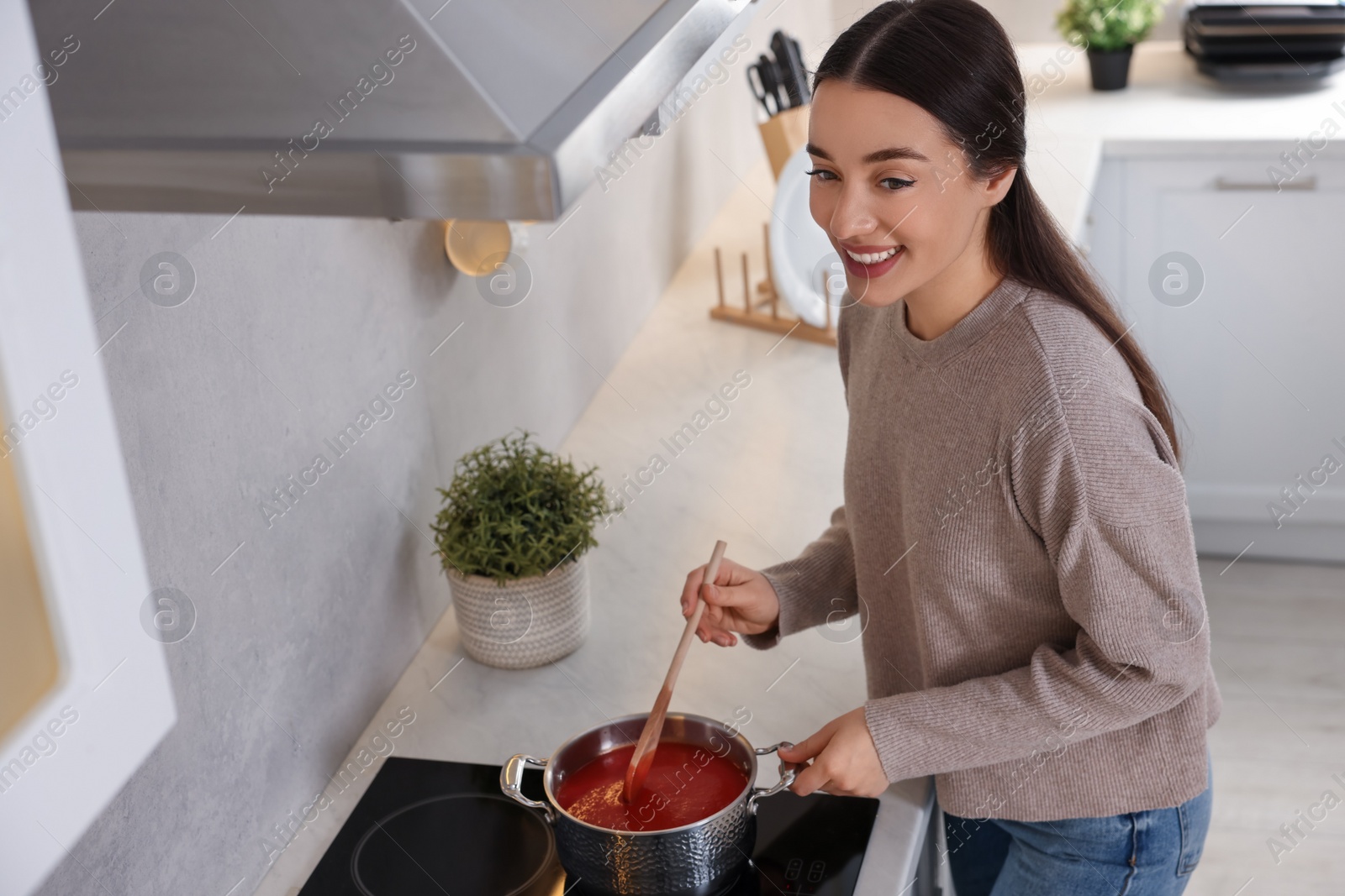 Photo of Smiling woman with wooden spoon cooking tomato soup in kitchen, above view. Space for text