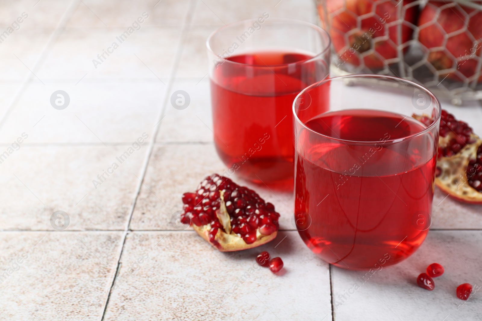 Photo of Tasty pomegranate juice in glasses and fresh fruits on white tiled table, closeup. Space for text