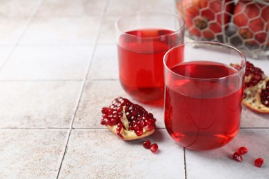 Photo of Tasty pomegranate juice in glasses and fresh fruits on white tiled table, closeup. Space for text