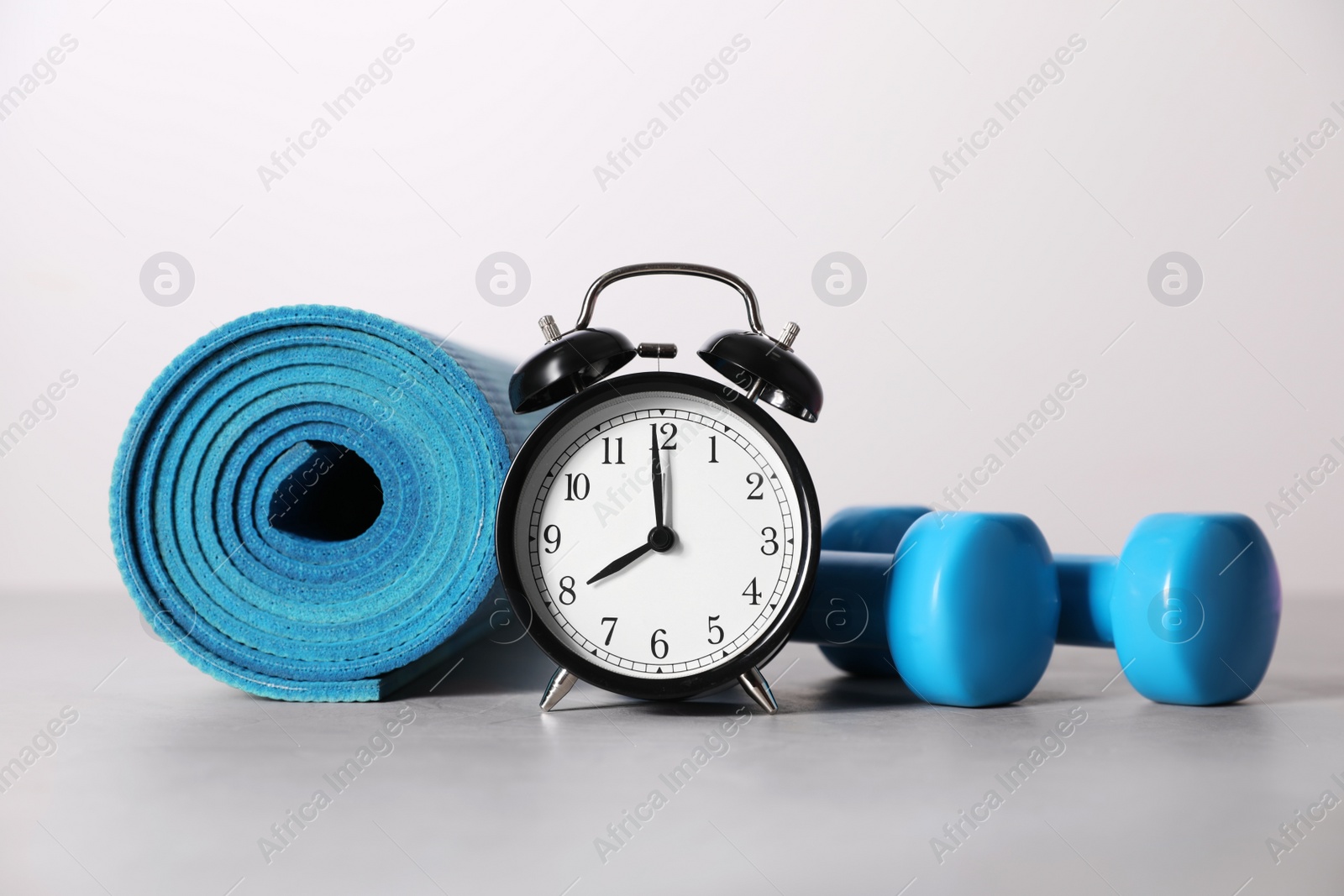 Photo of Alarm clock, yoga mat and dumbbells on grey background. Morning exercise