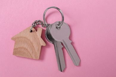 Photo of Metallic keys with wooden keychain in shape of house on pink background, top view. Space for text