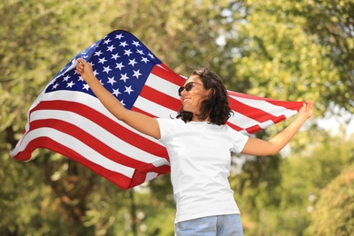 Happy young woman with American flag in park on sunny day