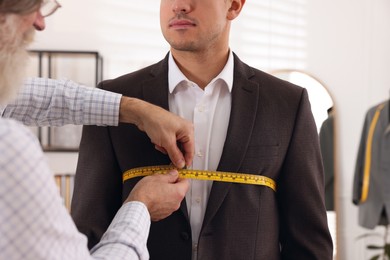 Photo of Professional tailor measuring client's chest circumference in atelier, closeup