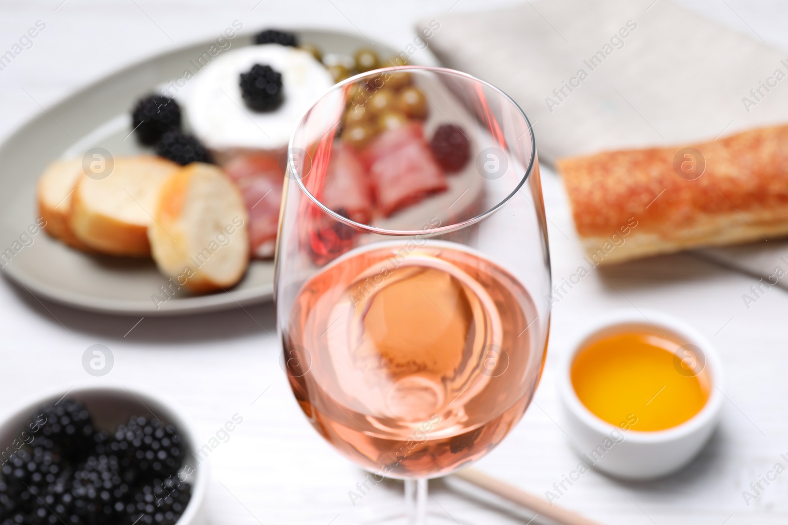 Photo of Glass of delicious rose wine and snacks on white table, closeup