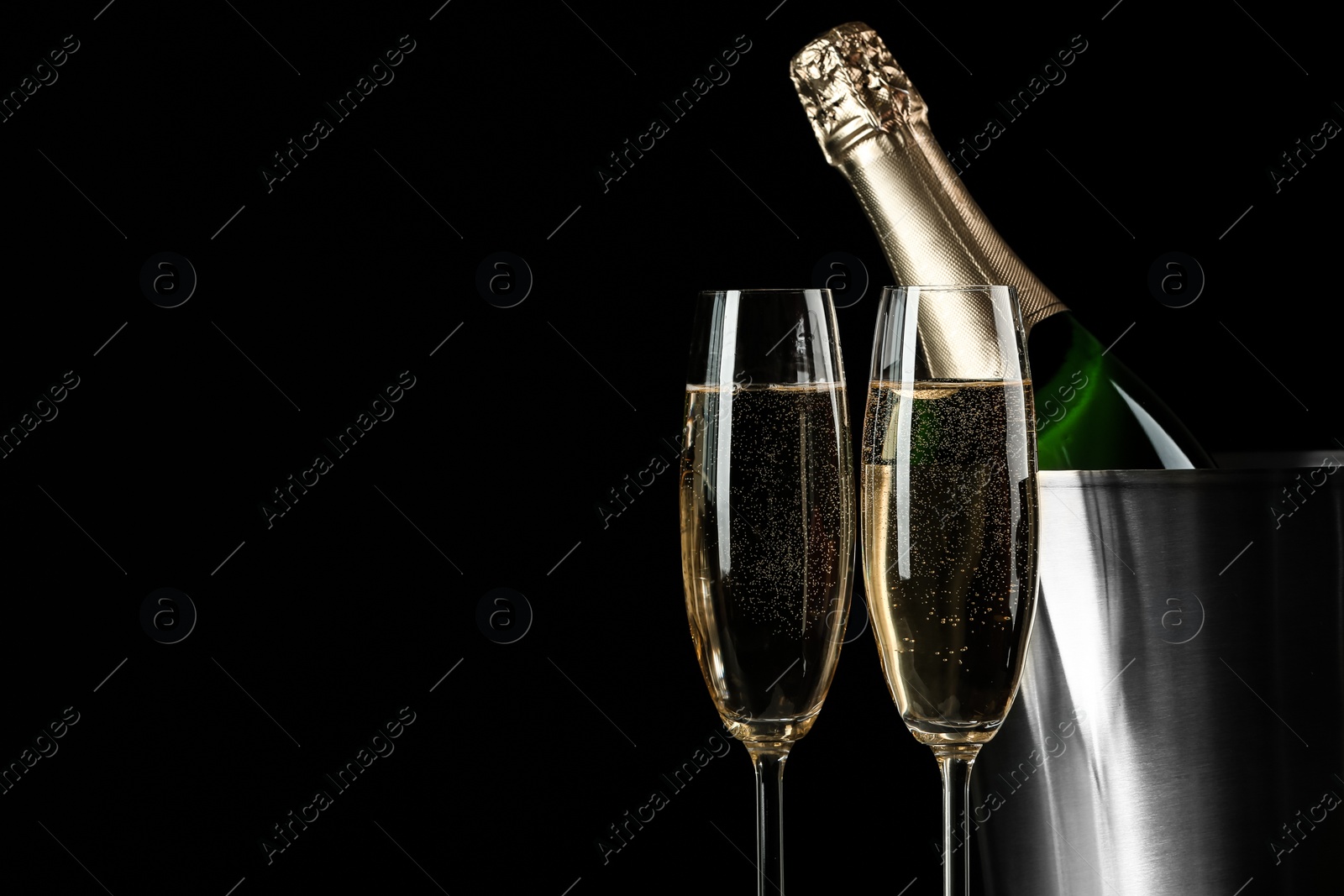 Photo of Glasses of champagne near bucket with bottle on black background, space for text