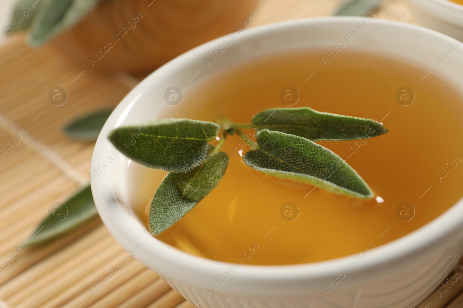 Photo of Cup of aromatic sage tea with fresh leaves on table, closeup