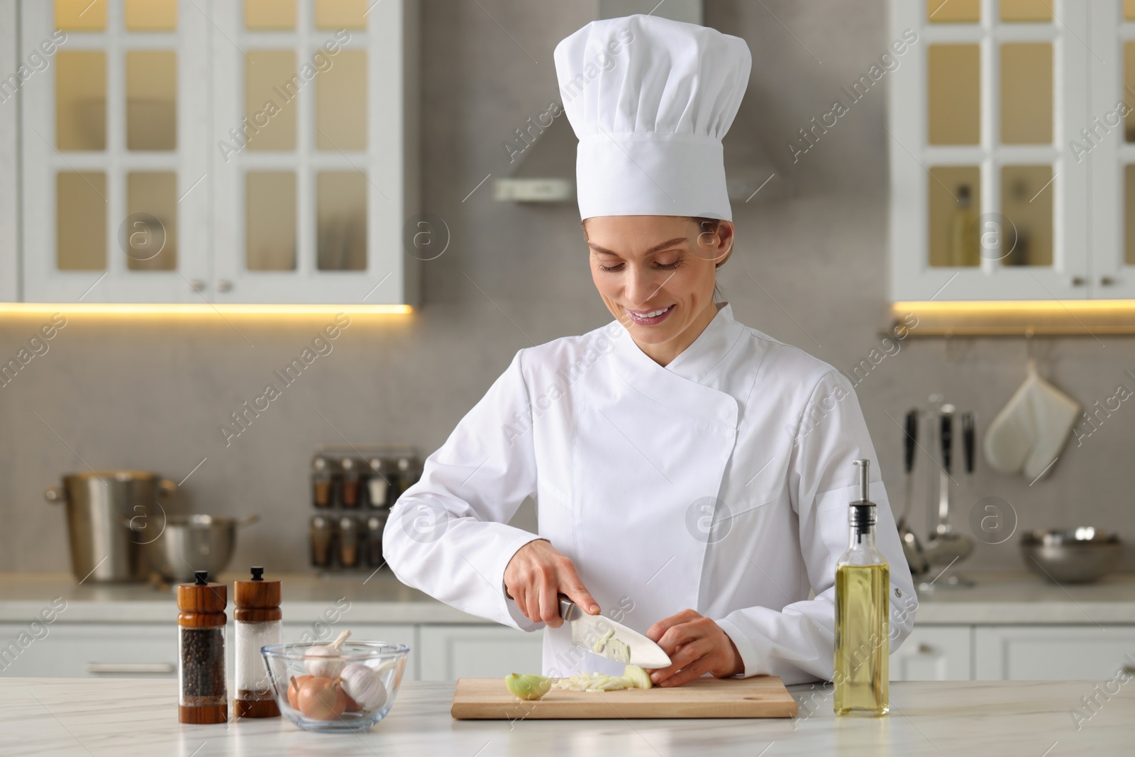 Photo of Professional chef cutting onion at white marble table indoors