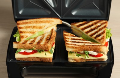 Photo of Modern grill maker with sandwiches on table, closeup view