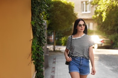 Beautiful young woman in stylish sunglasses walking on city street