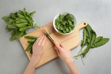 Photo of Woman cutting sorrel leaves at light grey table, top view