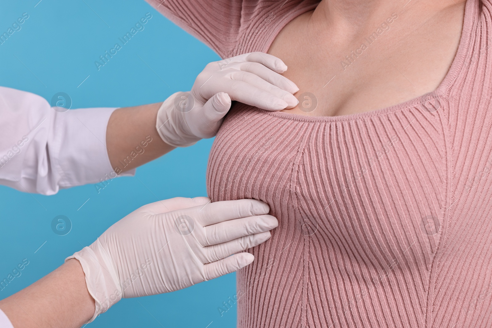 Photo of Mammologist checking woman's breast on light blue background, closeup