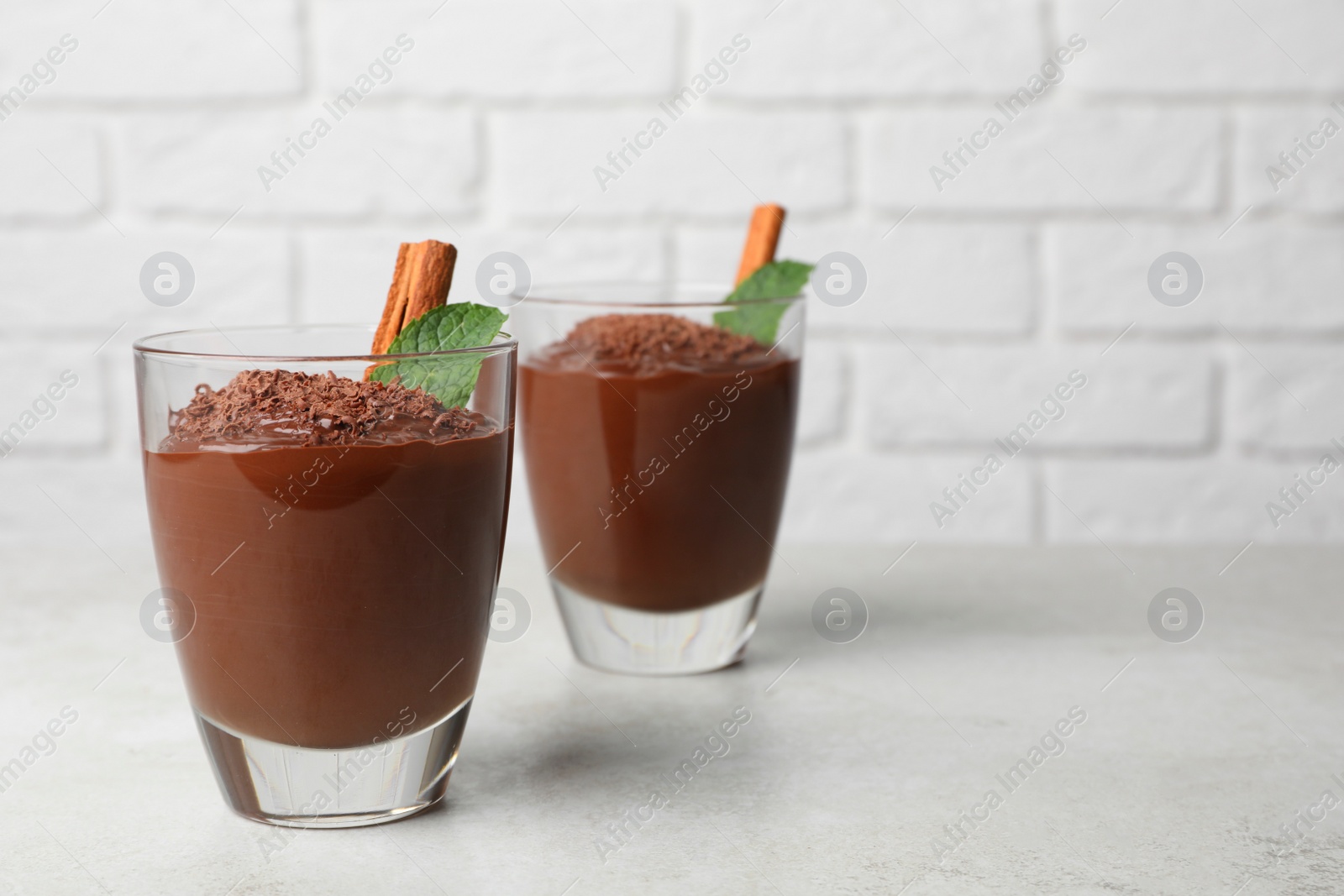 Photo of Cups of delicious hot chocolate with cinnamon stick and mint on light grey table near brick wall, space for text