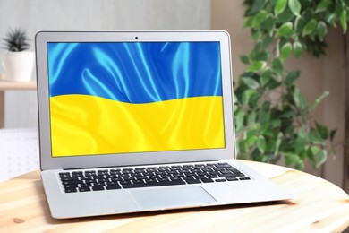 Image of Modern laptop with picture of Ukrainian national flag on screen indoors